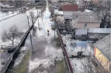  ?? DAVID GUTTENFELD­ER/THE NEW YORK TIMES ?? A resident walks down a flooded street Monday in Demydiv, a village north of Kyiv.