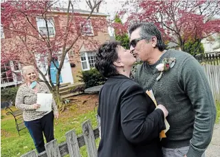  ?? OLIVIER DOULIERY AFP/GETTY IMAGES ?? A newly married couple kisses for the first time as husband and wife as the state marriage officiant who performed the ceremony watches from a safe distance in Arlington, Va., on Wednesday.