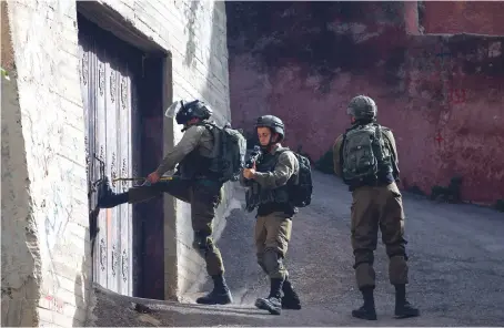  ?? AP ?? Israeli troops in the village of Aqraba, near the West Bank town of Nablus, try to break open a door during Tuesday’s search operation for a suspected Palestinia­n gunman.