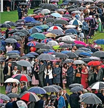  ?? ?? Pour folk: Garden party guests shelter under brollies as the heavens open