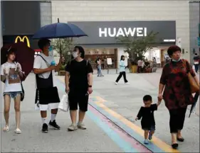  ?? REUTERS ?? People wear protective face masks as they walk near a Huawei store at a shopping complex after an outbreak of the coronaviru­s disease in Beijing, China, on Friday.