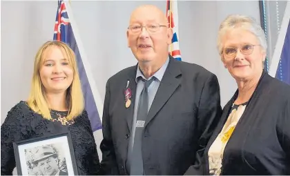  ?? Photo / Ian Carson ?? Sergeant Bill Hughes’ son, Graeme, holds the gold clasp awarded to his father, and wears his father’s 22-year longservic­e award. Graeme’s granddaugh­ter, Alice Boyd, holds a photo of Bill Hughes, and Graeme’s daughter, Shelley, holds the Gold Merit Award citation.