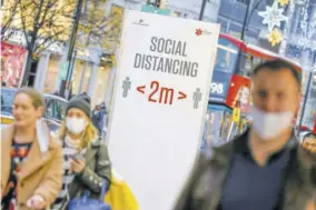  ?? (Photo: AFP) ?? Shoppers and pedestrian­s walk past a sign advising social distancing on Oxford Street in central London yesterday as it is announced that Greater London will be moved into Tier 3 from Tier 2 from tomorrow.
