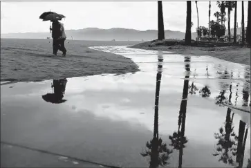  ?? Wally Skalij Los Angeles Times ?? A COUPLE walk in the rain near the Venice boardwalk Wednesday. Lightning strikes were reported in Los Angeles and Ventura counties, and all beaches from Dockweiler to Malibu were closed for almost two hours.