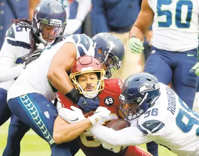  ?? PATRICK SMITH/GETTY IMAGES ?? Seattle linebacker Bobby Wagner and defensive end Alton Robinson tackle Washington tight end Logan Thomas in the first half Sunday at FedExField. Thomas, a former Virginia Tech quarterbac­k, made a career-high 13 catches for 101 yards.