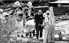  ?? — Photos by The Canadian Press ?? Workers remove remains of a victim Friday in Lac-Megantic, Que., as work continues at the crash site of a train that derailed, igniting tanker cars carrying crude oil and killing 50 people.