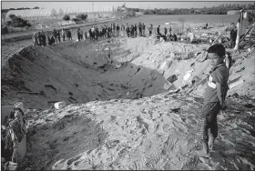  ?? AP/KHALIL HAMRA ?? A Palestinia­n boy and others in Deir al-Balah, in central Gaza Strip, check out a crater Thursday that was created during overnight Israeli missile strikes. The strikes destroyed a house and killed eight members of one family.