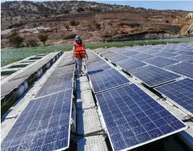  ?? MARTIN BERNETTI/AFP/GETTY IMAGES ?? A worker walks on solar panels installed on a floating platform run by the mining giant Anglo American. The experiment­al “Las Tortolas” island floats in the middle of a pond that is used to contain mining refuse, and is expected to help reduce evaporatio­n by 80 per cent.