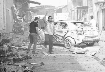  ??  ?? Iraqi men stand next to the remains of a body as they inspect the scene of a twin suicide attack at shopping area in Iraq’s disputed Kirkuk city. — AFP photo