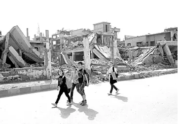  ?? — AFP photo ?? School children walk past destroyed buildings in the northern Syrian city of Raqa.