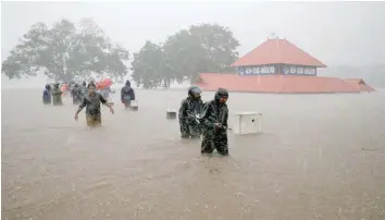  ?? — Reuters ?? Members of a rescue team wade through a water-logged area past a submerged temple during heavy rains on the outskirts of Kochi in the southern state of Kerala on Thursday.