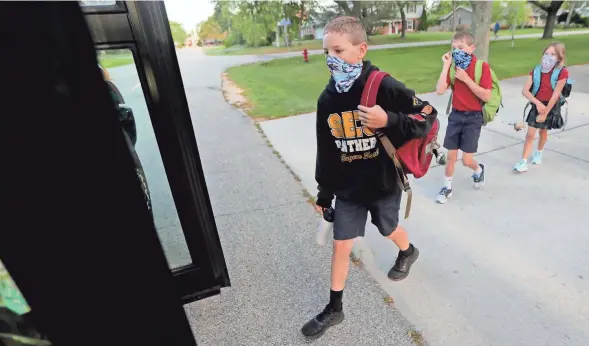  ?? MIKE DE SISTI / MILWAUKEE JOURNAL SENTINEL ?? Isaac Tomczuk, 12, in seventh grade; his brother, Luke, 9, in third grade; and their sister, Cecelia, 6, in first grade, board a bus for their first day of school Aug. 31, 2020, outside their home in Bayside. The children are students at St. Eugene School in Fox Point.