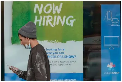  ?? (AP/Tony Dejak) ?? A man walks past a “Now Hiring” sign on a window at a Sherwin-Williams store in Woodmere Village, Ohio, last month. Applicatio­ns for unemployme­nt benefits fell more than forecast last week to the lowest since early November.
