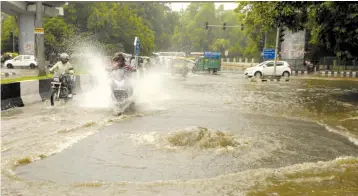  ?? — PRITAM BANDYOPADH­YAY ?? A biker try to negotiate on a waterlogge­d road near R. K. Ashram Metro Station after heavy rain in New Delhi on Sunday.