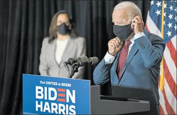  ?? CAROLYN KASTER/AP ?? With running mate Sen. Kamala Harris watching, Democratic presidenti­al candidate Joe Biden replaces his face mask after speaking Thursday in Wilmington, Delaware.