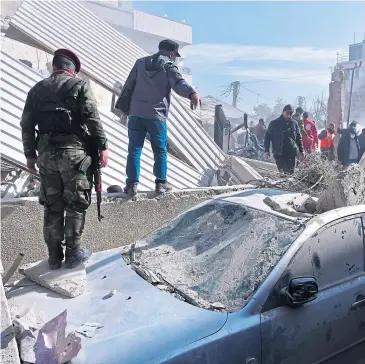  ?? ?? Soldiers and locals check a damaged car at the site of the building hit by an air strike in Damascus.