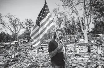  ?? John Locher / Associated Press ?? Freddie Cox carries a flag Sunday to plant at the charred remains of the home of his godfather, Ed Bledsoe, in Redding, Calif. Bledsoe’s wife, Melody, great-grandson James Roberts and great-granddaugh­ter Emily Roberts were killed at the home in the Carr Fire.