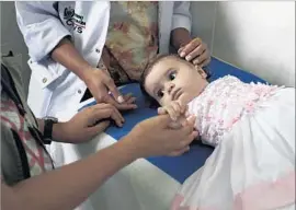  ??  ?? SIX-MONTH-OLD Eloisa de Oclaceo, who does not have microcepha­ly, holds a doctor’s hand as a nurse strokes her head before she has blood drawn.