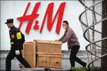  ?? MARK SCHIEFELBE­IN / AP ?? A security guard helps a worker move boxes past an H&M clothing store at a shopping mall in Beijing on Friday.