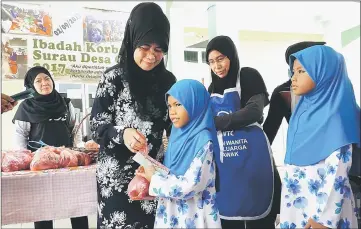  ??  ?? Fatimah (left) distribute­s packets of sacrificia­l meat to the children.
