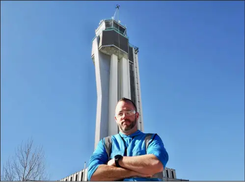  ?? PHOTOS BY MATT GEIGER — BUSINESSDE­N ?? Jay Hanna, co-owner of Drone Wash, poses in front of the Flyteco tower while “Betty,” his cleaning drone, goes to work on the building’s observatio­n deck.