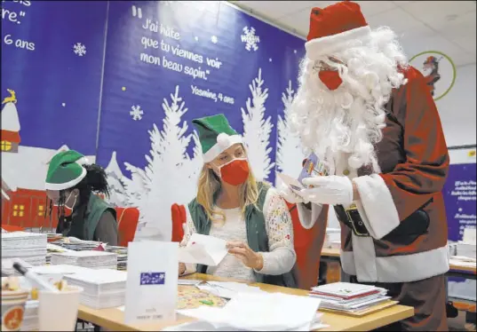  ?? Francois Mori The Associated Press ?? A postal worker dressed as Santa talks with co-workers as they open envelopes addressed to Père Noël, Father Christmas in French, in Libourne, France on Monday. The letters offer a glimpse into the worries and hopes of children during the pandemic.