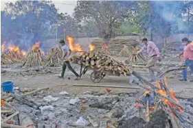  ?? AP PHOTO/ISHANT CHAUHAN ?? A worker carries wood on a hand cart as multiple funeral pyres of COVID-19 victims burn Saturday at a crematoriu­m on the outskirts of New Delhi, India.