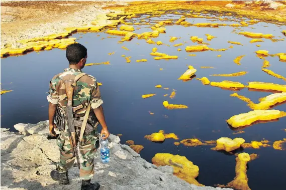  ?? PHOTOS: PAUL SCHEMM/THE WASHINGTON POST ?? An Ethiopian guard looks across the brightly coloured sulphur springs in the country’s sweltering Afar Region.