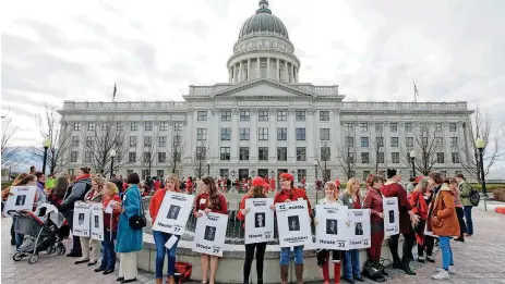  ?? [AP PHOTOS] ?? Women dressed in red and holding signs with photos of their local lawmakers are gathered at the Utah state capitol Wednesday for a Day Without a Woman protest.