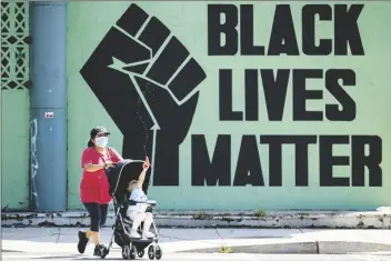  ?? HARNIK/AP ANDREW ?? A girl in a stroller plays with a squirt gun as a woman pushes her past a Black Lives Matter mural in the Shaw neighborho­od in Washington, on Monday.