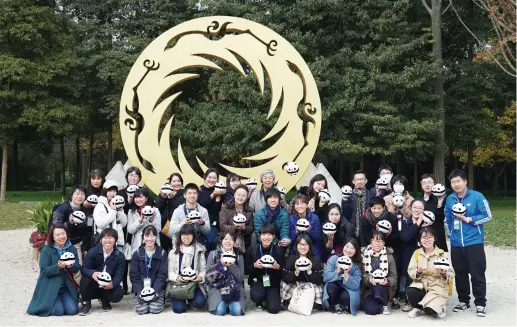  ??  ?? 「太陽神鳥」の像の下で、パンダのぬいぐるみを­持つ訪中団一行（写真・任川）