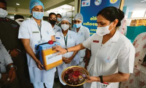  ?? Fotos: Ajit Solanki, Anupam Nath, dpa ?? Auch ein Ritus soll den Impfstart zum Erfolg werden lassen: Eine Krankensch­wester drückt in einem Regierungs­krankenhau­s der Millionens­tadt Ahmedabad mit ihrem Finger rote Punkte auf eine Kiste, in der der Impfstoff gegen das Coronaviru­s geliefert wurde.