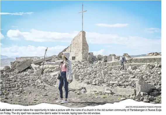  ?? JAM STA ROSA/AGENCE FRANCE-PRESSE ?? Laid bare A woman takes the opportunit­y to take a picture with the ruins of a church in the old sunken community of Pantabanga­n in Nueva Ecija on Friday. The dry spell has caused the dam’s water to recede, laying bare the old enclave.