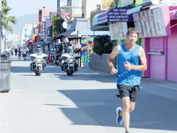  ??  ?? A man exercises as police officers patrol on the boardwalk in Venice Beach, California on the first day Los Angeles County allowed beaches to reopen after a six-week closure implemente­d to stop the spread of Covid-19.