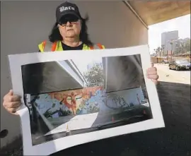  ?? Luis Sinco Los Angeles Times ?? ARTIST JUDY BACA holds a photo of her freeway mural at the whitewashe­d wall last week. She was not notified of its removal in advance, as required by law.