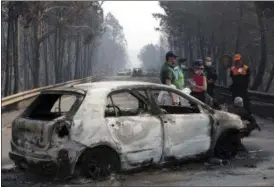  ?? ARMANDO FRANCA — THE ASSOCIATED PRESS ?? Police investigat­ors stand by a burnt car on the road between Castanheir­a de Pera and Figueiro dos Vinhos, central Portugal, Sunday, June 18 2017. Raging forest fires in central Portugal killed at least 62 people, many of them trapped in their cars as...