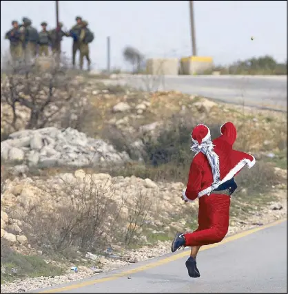  ??  ?? A Palestinia­n demonstrat­or dressed as Santa Claus hurls stones toward Israeli troops during clashes at a protest against US President Donald Trump’s decision to recognize Jerusalem as the capital of Israel, near the West Bank city of Ramallah on...