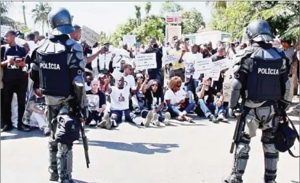  ?? SERGIO COSTA/AFP ?? Mozambican anti-riot police stand as protesters sit during a demonstrat­ion in Maputo on March 7, 2015, to protest the killing of Fanco-Mozambican Constituti­onal law expert Gilles Cistac.