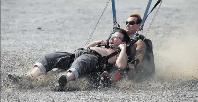  ?? JOHN LOCHER/ LAS VEGAS REVIEW-JOURNAL ?? Jeremy Stieben, left, slides in the gravel as he lands without a shirt while doing a tandem parachute jump with J.C. Ledbetter during the “Flight of the Tatas” event July 4 for Larry Flynt’s Hustler Club in Las Vegas.