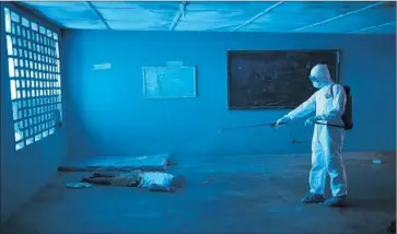  ?? Johnmoore Getty Images ?? worker in August disinfects the body of a man who died in a classroom that had been transforme­d into an Ebola isolation ward in the capital, Monrovia.