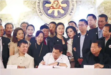  ?? AP FOTO ?? NEW LAWS. President Rodrigo Duterte, center, leads the ceremonial signing of the 2018 General Appropriat­ions Act and Tax Reform for Accelerati­on and Inclusion Act as members of Congress stand behind him in Malacañang.