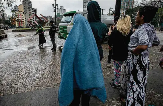  ??  ?? Moradores de rua observam limpeza da praça da Sé, no centro de SP, na manhã desta quinta (20)