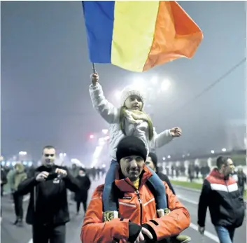  ?? DANIEL MIHAILESCU/ GETTY IMAGES ?? A man carries a girl waving a Romanian flag in front of the Romanian parliament during a protest of the government and corruption in Bucharest on Sunday. Citizens are expected to forego the festivitie­s of the country’s Dec. 1 national holiday, and...