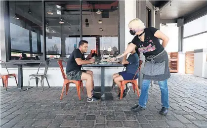  ?? RICARDO RAMIREZ BUXEDA/ORLANDO SENTINEL ?? Jonathan Ysea and Klarissa Hopton sit in the patio as Christina Bishop brings in their order at Hawkers Asian Street Fare in Orlando on July 9.