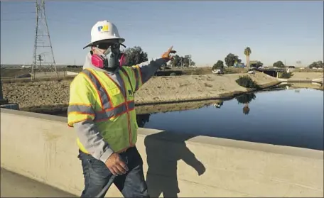  ?? Carolyn Cole Los Angeles Times ?? AN INVESTIGAT­OR from the Los Angeles County Department of Public Works wears a mask to block the noxious smell from the Dominguez Channel in Carson. Residents have reported headaches and nausea and have had to keep their doors and windows closed.