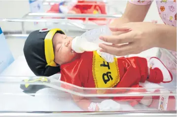  ?? PATIPAT JANTHONG ?? A Paolo Memorial Hospital nurse feeds a newborn in a special costume prepared by the hospital for the Chinese New Year. Parents get child allowance deductions for an unlimited number of biological children under the new personal income tax rules.