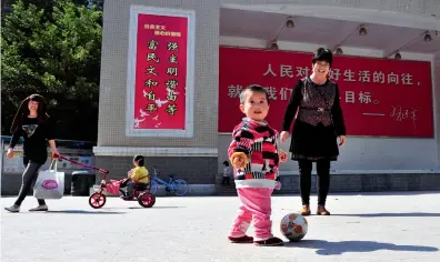  ??  ?? Children play freely while their family members look after them on Nanling Village Recreation and Sports Central Square in Shenzhen, Guangdong Province on February 15, 2017. The huge poster in the background shows the socialist core values.