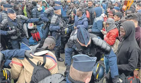  ?? Picture: PA. ?? French police officers go in to stop a fight among a large crowd of migrants as they line up at a processing centre in the ‘Jungle’ near Calais, northern France, as the mass exodus from the migrant camp begins.