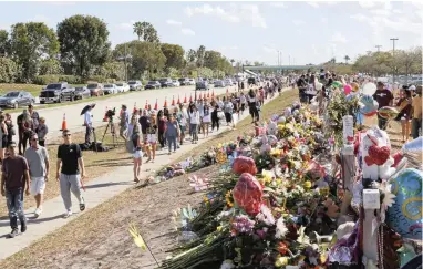  ?? PICTURE: AP ?? MEMORIAL: Parents and students walk next to the memorial for the victims of the shooting at Marjory Stoneman Douglas High School. It was an open house on Sunday as parents and students returned to the school for the first time since 17 victims were...
