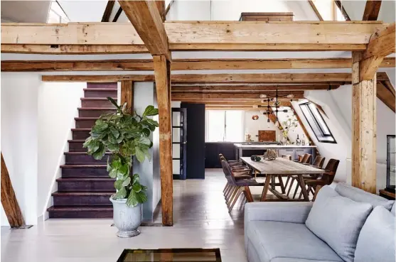  ??  ?? Living area The second of a matching pair of ‘Sweder’ sofas from Interiors DMF sits in front of a bespoke oak bookshelf designed by Nicemakers. The coffee table and console behind the sofa are both antique finds. On the wall hangs a vast wooden wheel, once used to haul belongings into the upper mezzanine level, which was at one time a storage area for the whole building Dining area A custom-made oak table with grass detailing takes inspiratio­n from the beams above. The chairs are from Project99, a Dutch
company that upcycles salvaged seats, while the light is a ‘Molecular’ pendant by House Doctor